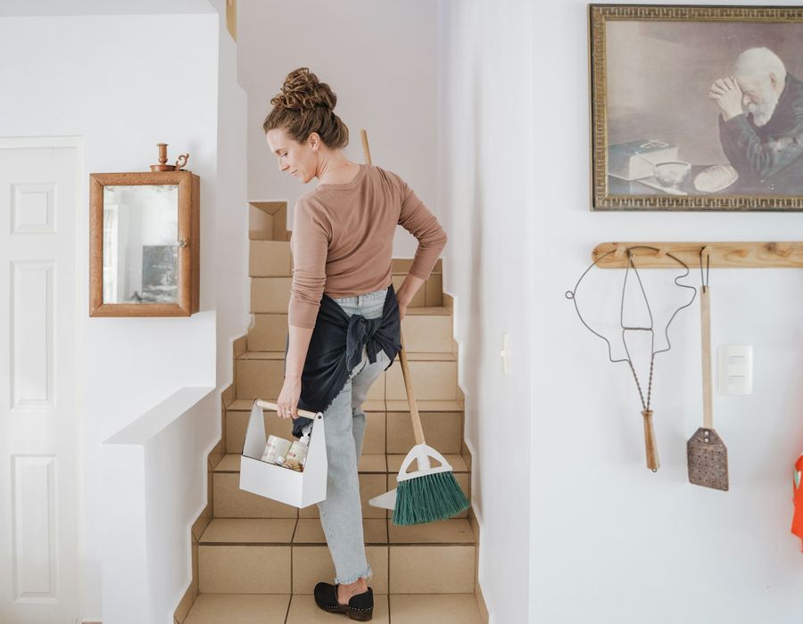 Cleaner carrying a cleaning caddy and broom up the stairs